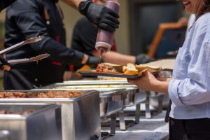 Guest being served Texas smoked BBQ with sauce at outdoor catering buffet