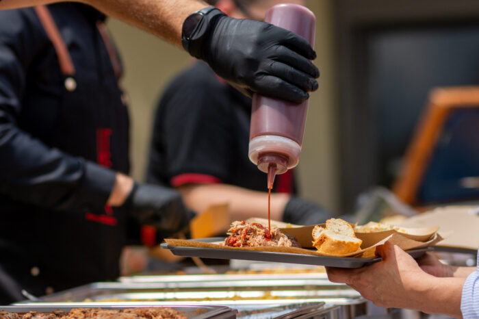 Close-up of BBQ chef adding sauce to smoked pulled pork at catering