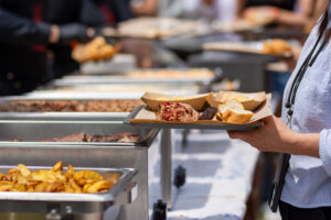 Guest holding plate with Texas BBQ brisket, bread, and sides at buffet