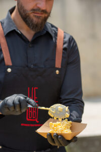 BBQ chef serving creamy mac and cheese at Texas smoked BBQ catering event