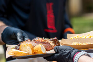 Plate with sliced smoked brisket, pulled pork, bread and sides at BBQ event